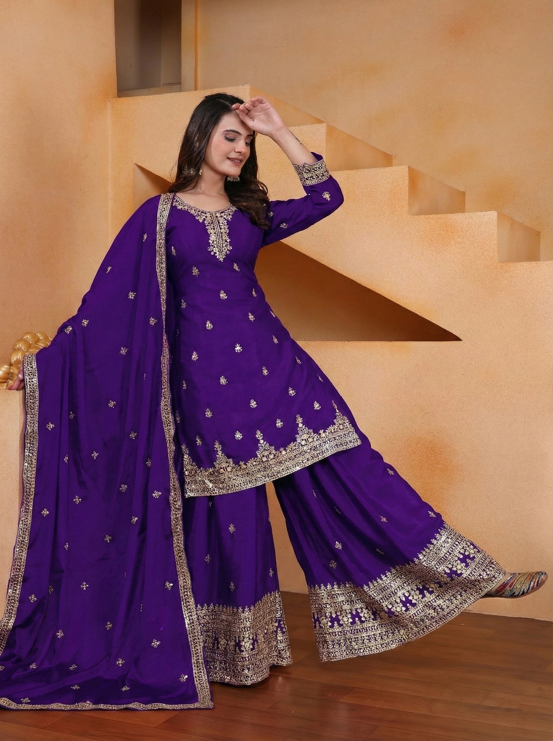 Woman in a purple traditional outfit with gold embroidery standing in front of a staircase.