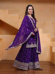 Woman wearing a purple traditional outfit with intricate designs in a warm-toned room.