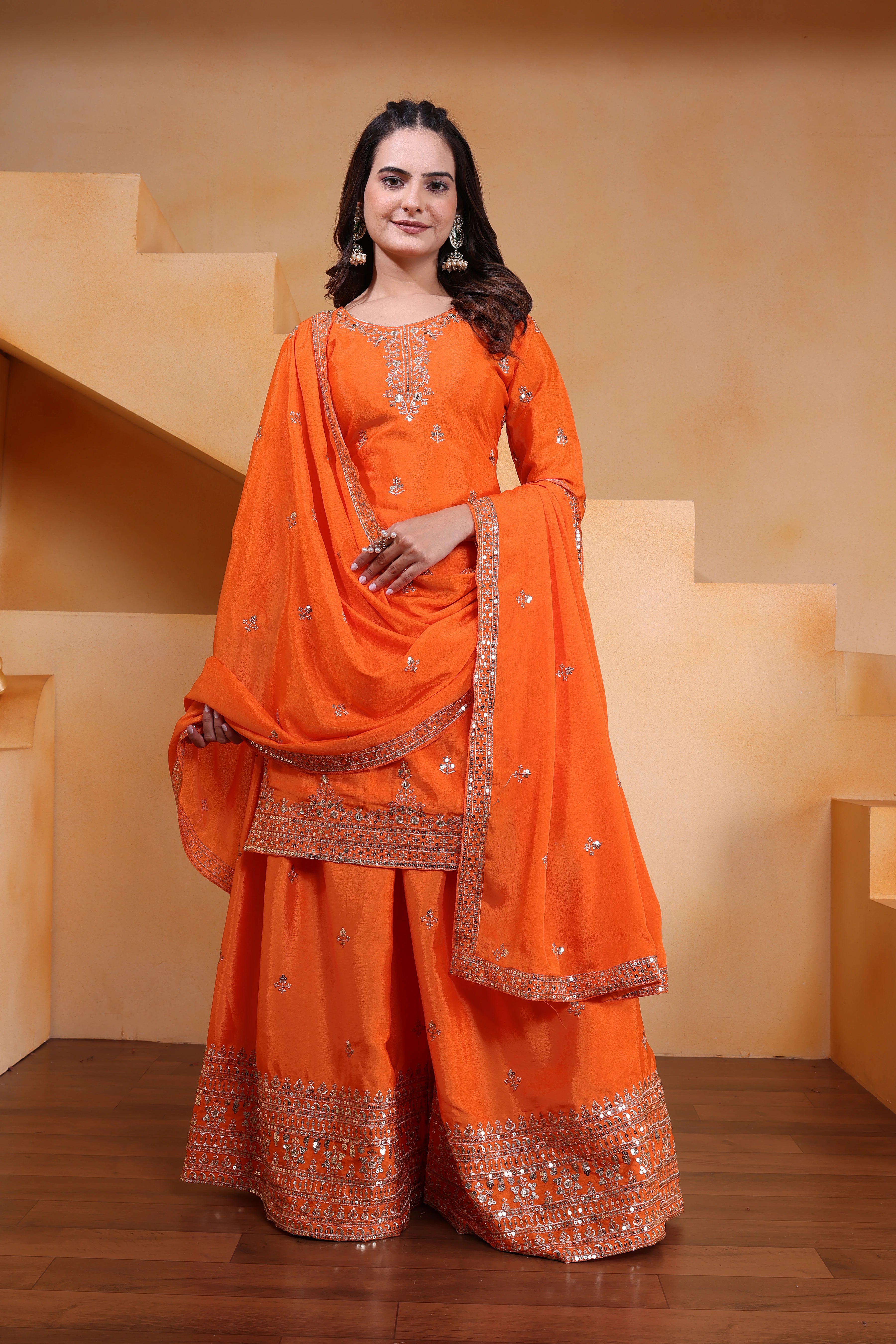 Woman in an orange traditional outfit with embroidery standing on a wooden floor.
