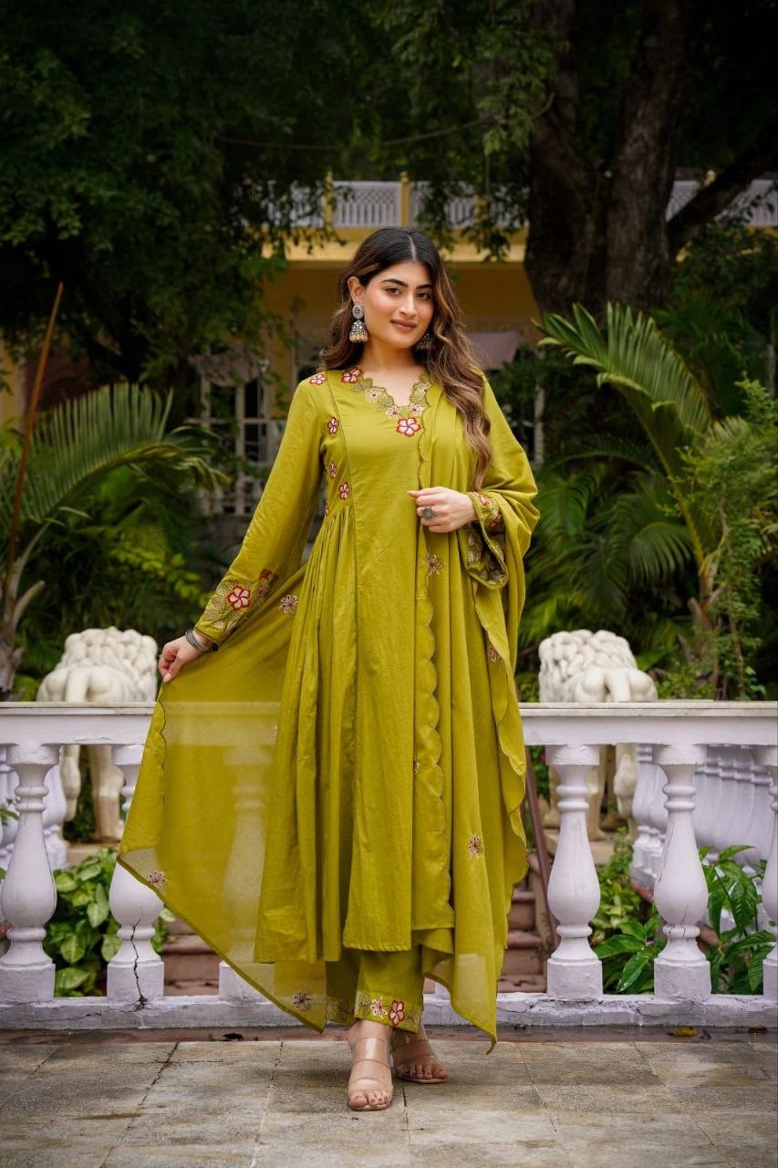 Woman in a green traditional outfit standing outdoors with greenery in the background