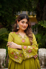 Woman in a green traditional outfit with floral embroidery standing outdoors.
