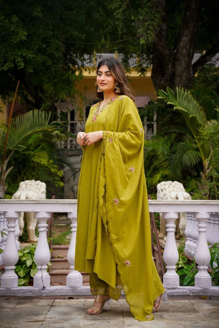 Woman in a green traditional outfit standing outdoors with greenery in the background