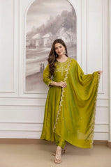 Woman in a green traditional outfit standing in a room with white walls and a framed picture.