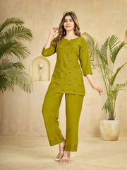 Woman wearing a green traditional outfit with plants in the background