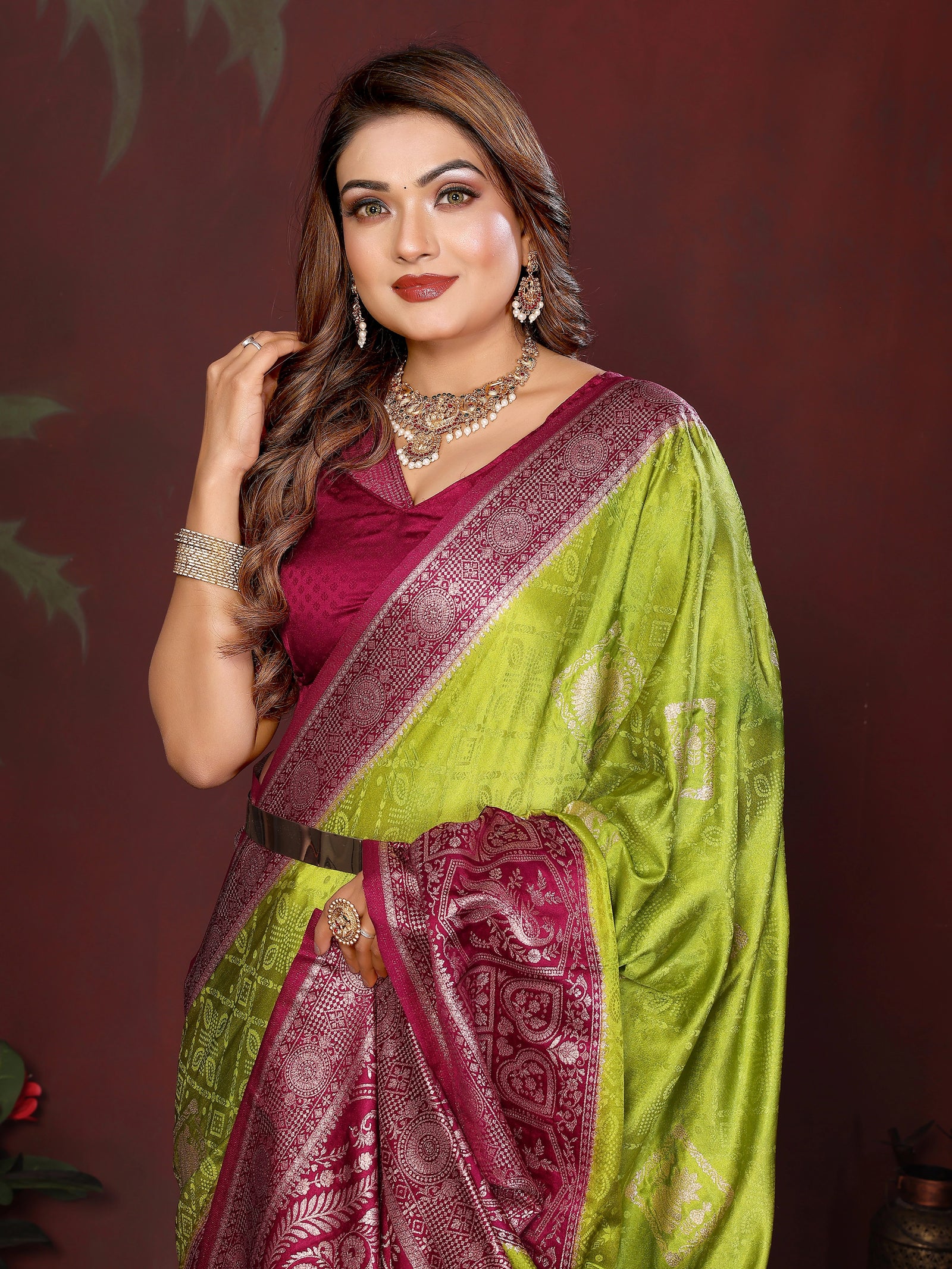Woman wearing a green and pink saree with jewelry against a dark background