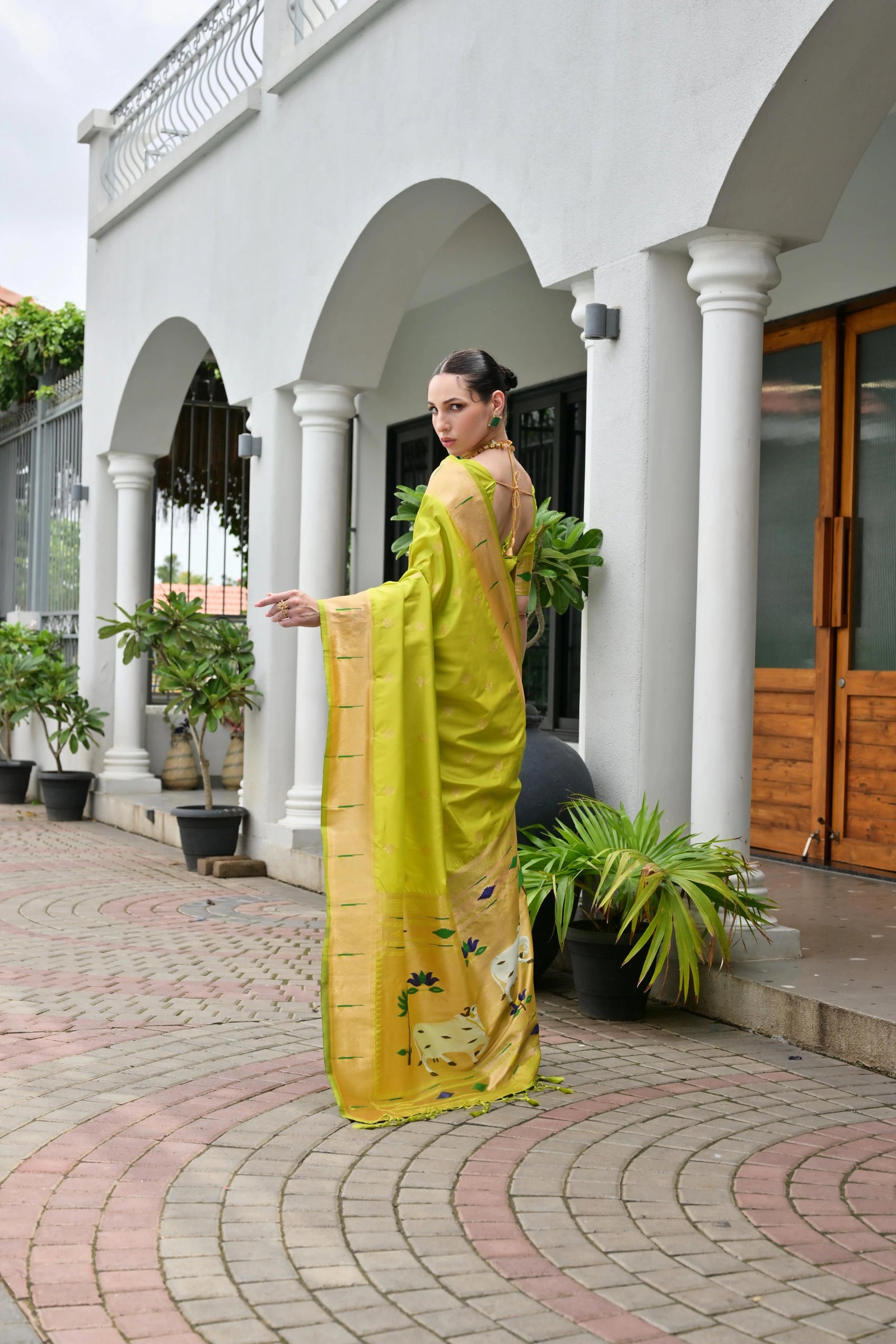 Woman in a yellow saree standing in front of a white building with columns.