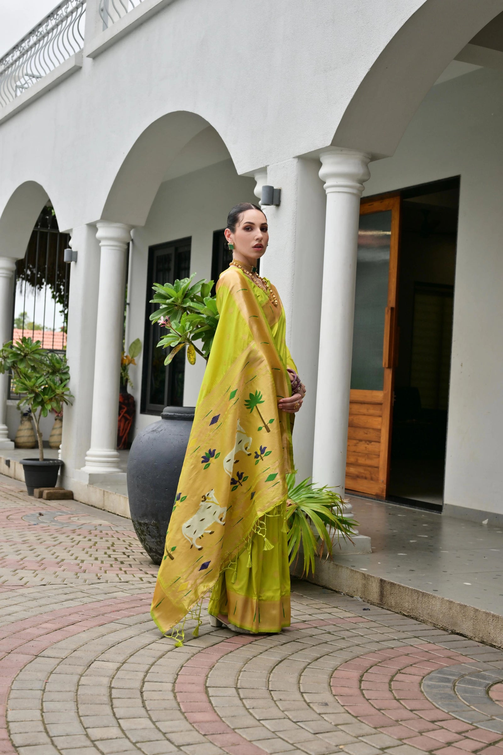 Woman in a yellow and green traditional outfit standing in front of a white building with arches.