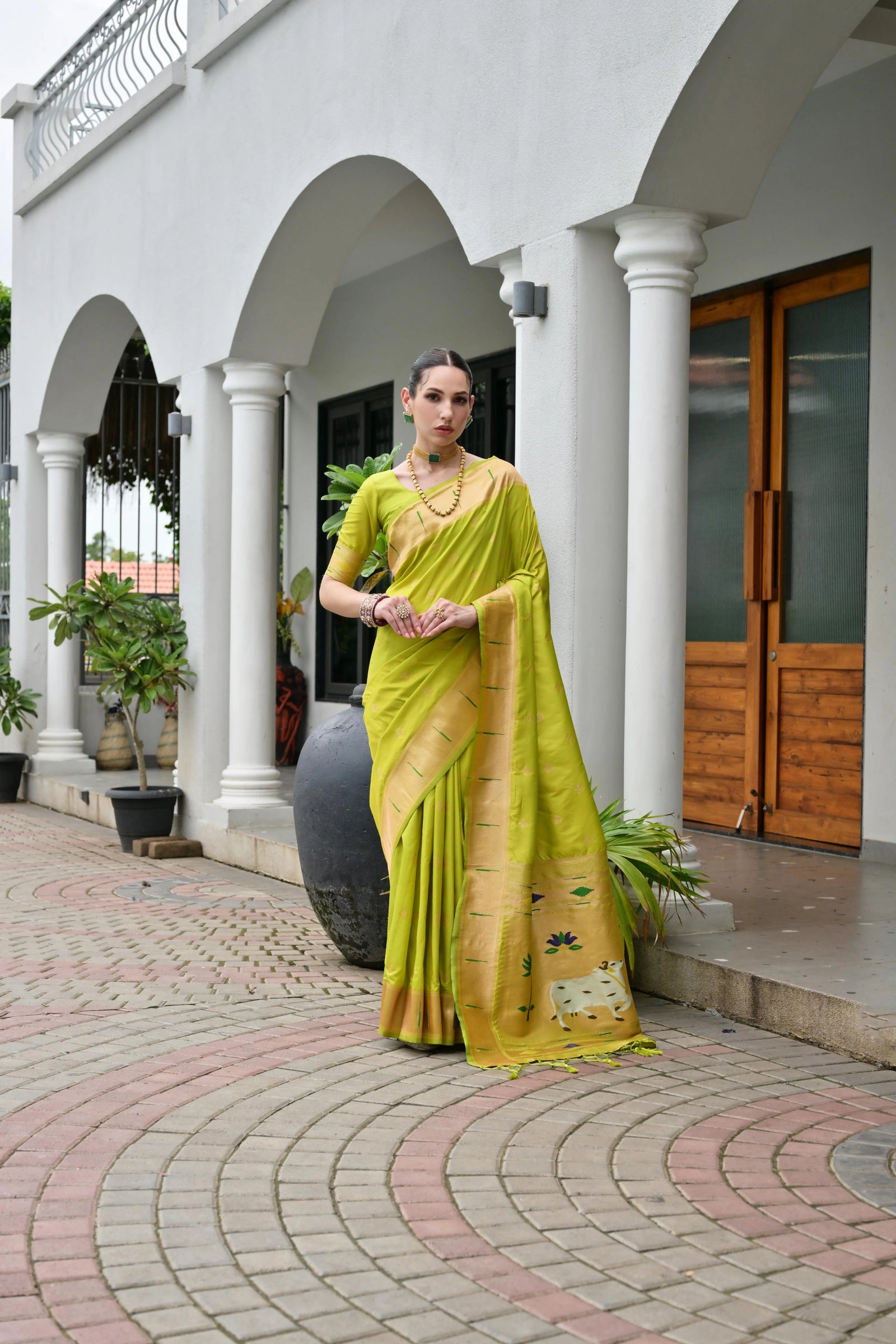 Woman in a yellow saree standing in front of a building with columns.