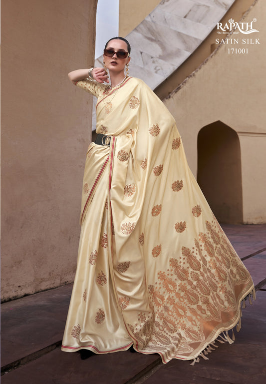Woman wearing a cream saree with gold patterns in an architectural setting, with 'Rajpath' branding.