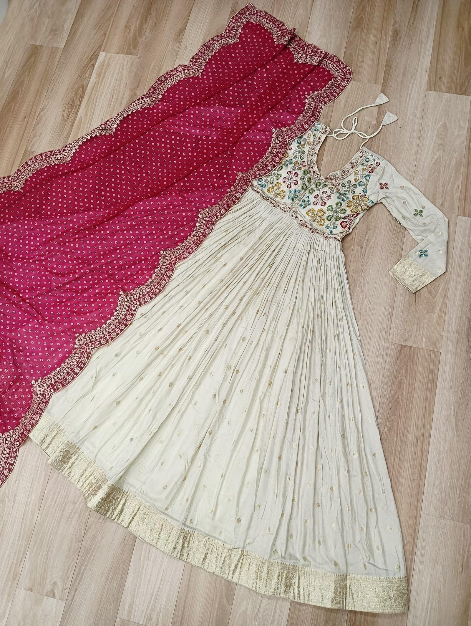 White traditional dress with floral patterns and a red dupatta on a wooden floor.