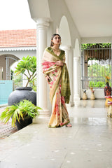 Woman in a colorful saree standing in front of a white archway with greenery in the background.
