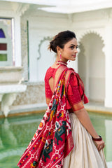 Woman in a red saree with a colorful pattern, standing in an elegant indoor setting.