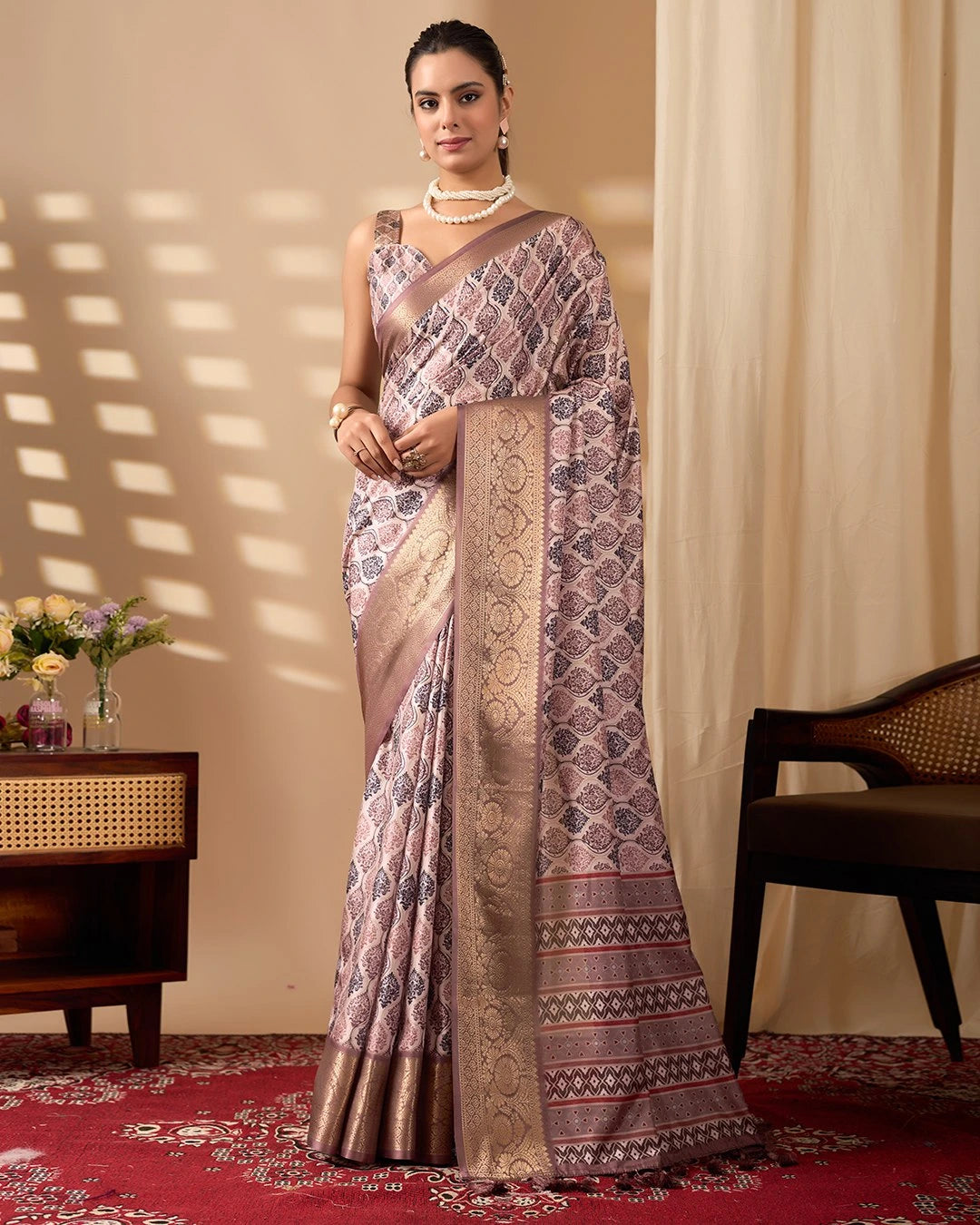 Woman wearing a patterned saree in a room with a chair and table.