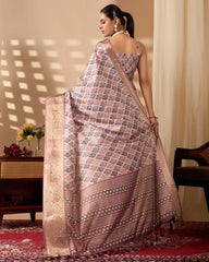 Woman wearing a patterned saree in a room with a table and flowers.