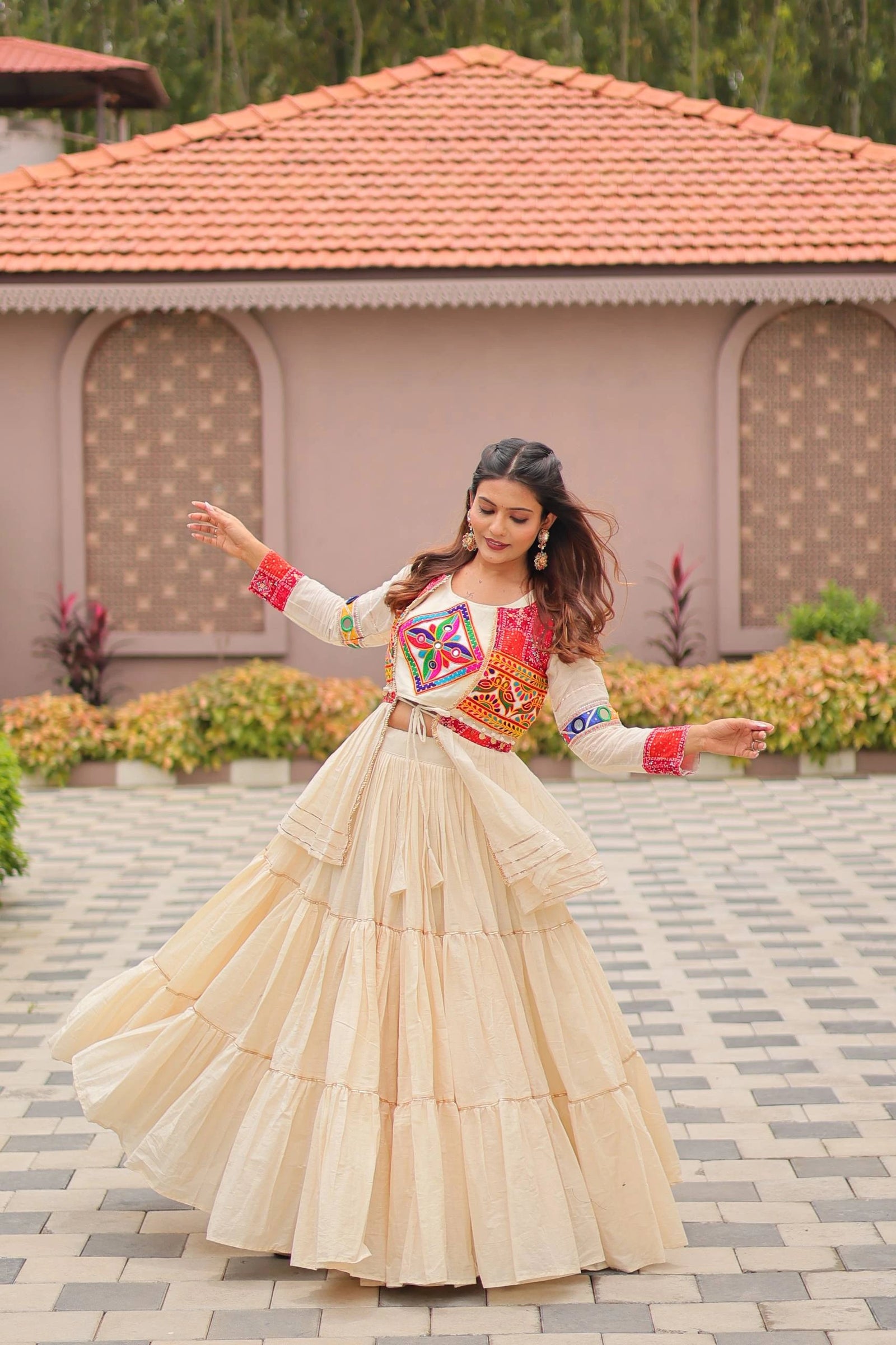 Woman in traditional outfit with colorful blouse and beige skirt standing on a paved area.