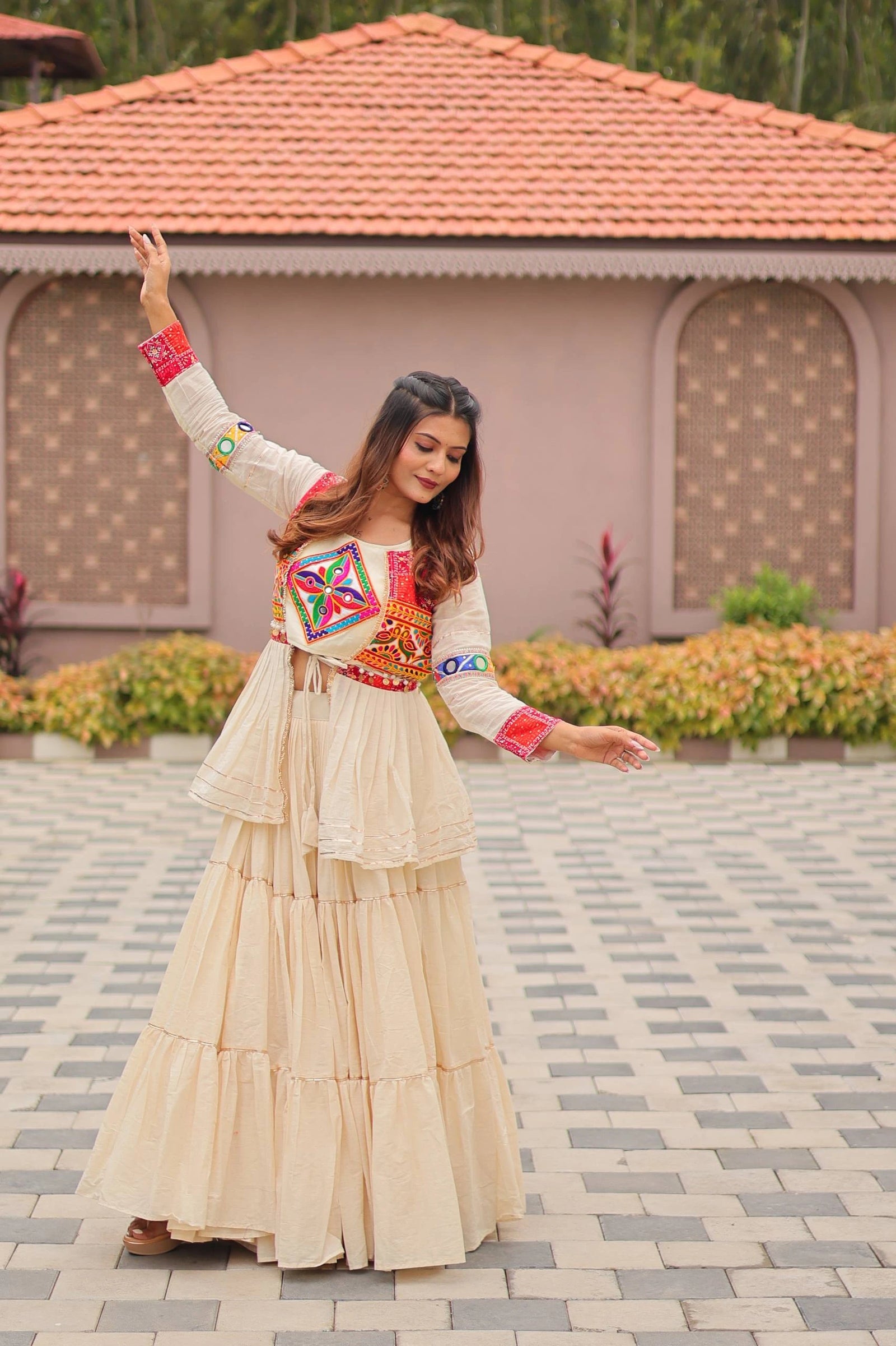 Woman in traditional outfit dancing outdoors with a house and garden in the background