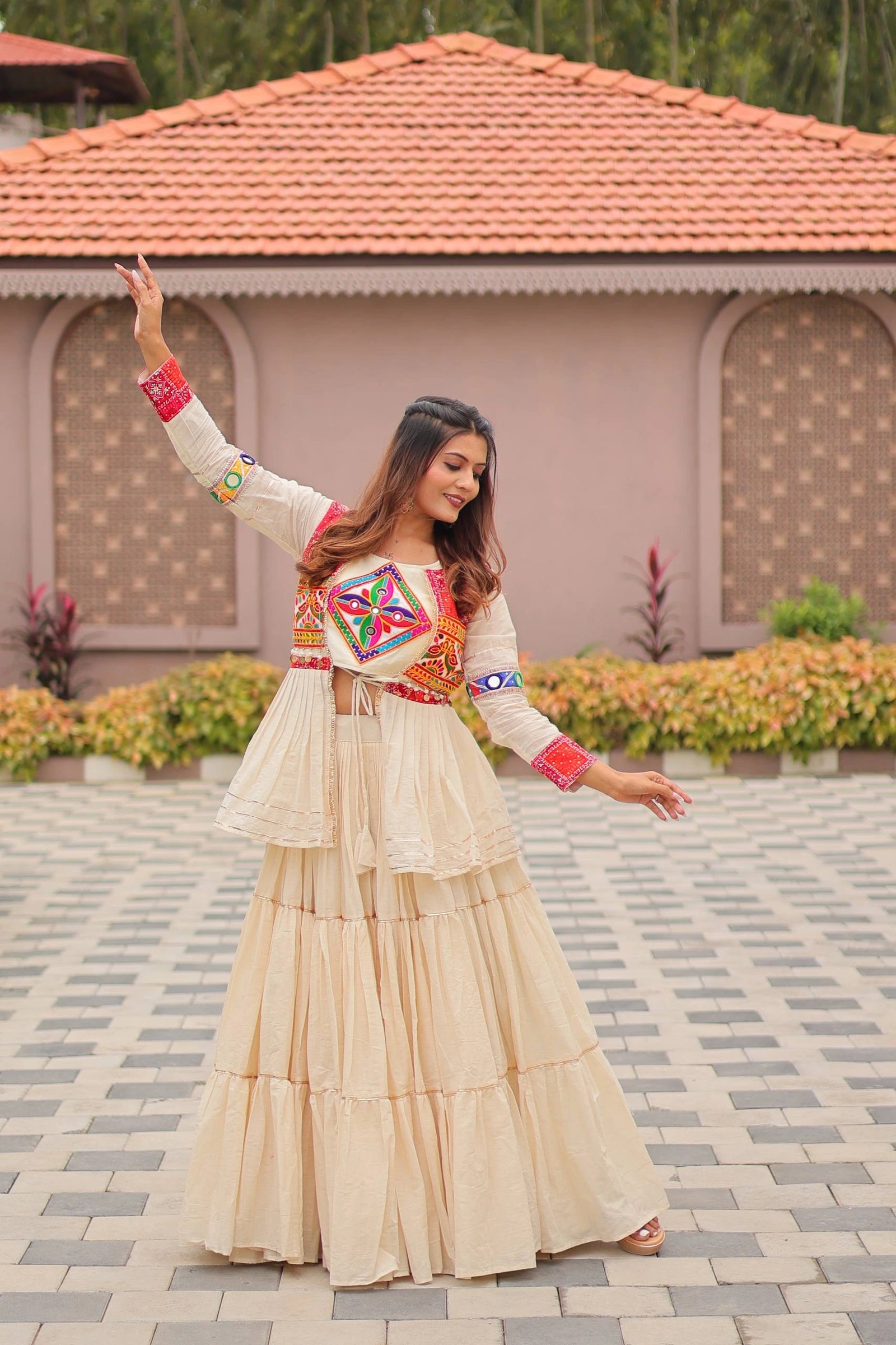 Woman in traditional outfit with colorful top and beige skirt standing on a paved area.