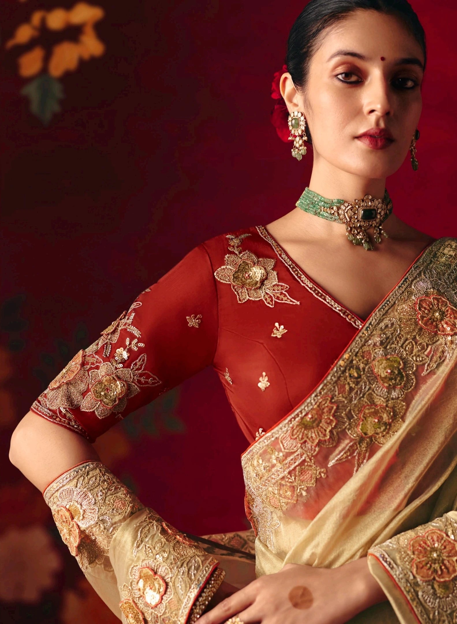 Woman wearing a traditional red and gold saree with intricate designs against a dark background