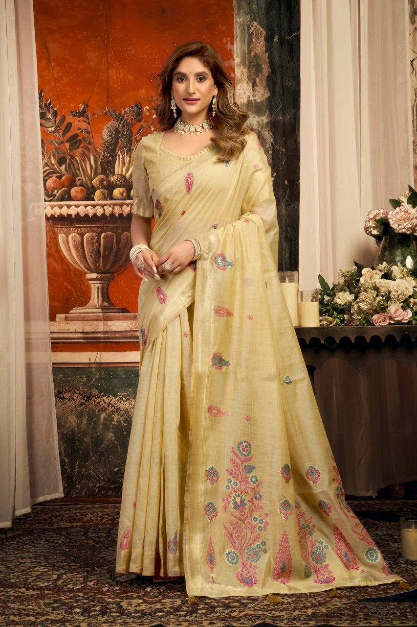 Woman in a cream saree with floral patterns standing in an elegant indoor setting.