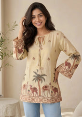 Woman wearing a beige embroidered tunic with palm trees and camels, standing indoors.