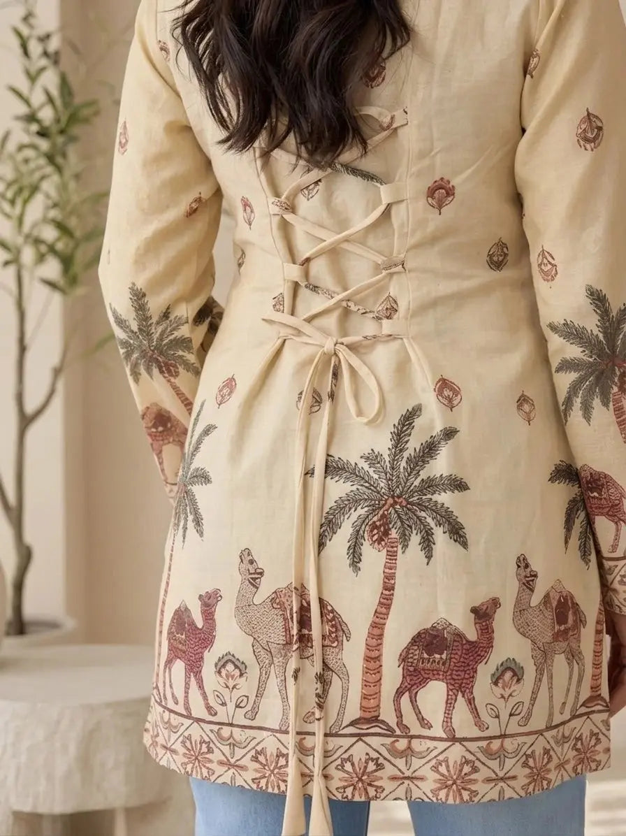 Beige coat with palm tree and camel pattern worn by a person indoors.