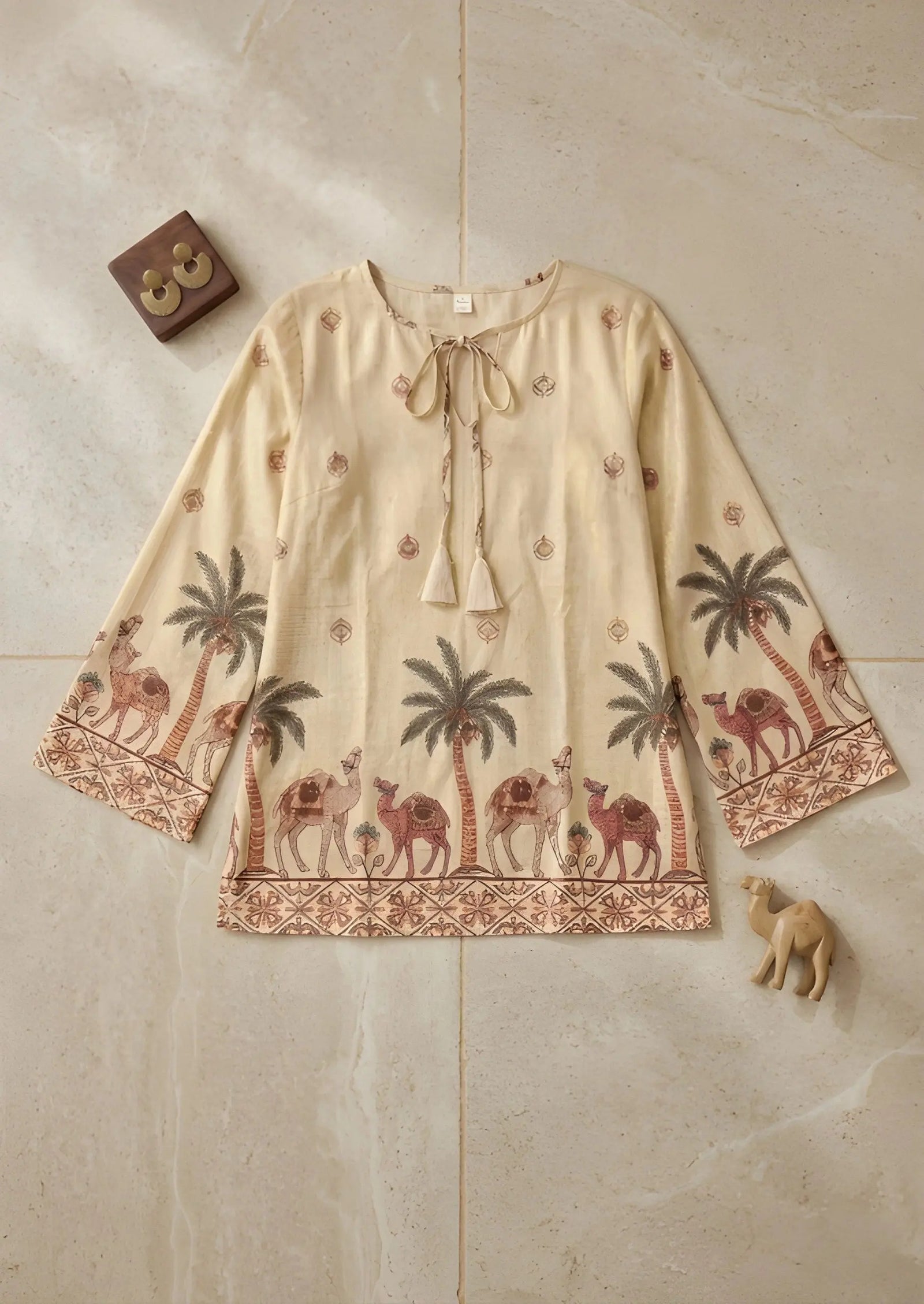 Beige blouse with camel and palm tree pattern on a beige tiled background