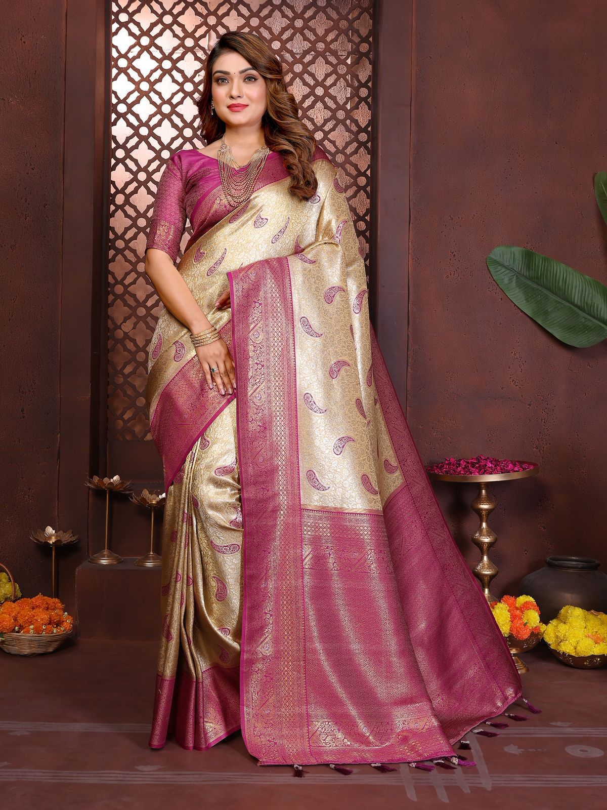Woman wearing a traditional saree with a pink and white patterned design, standing against a decorative background.