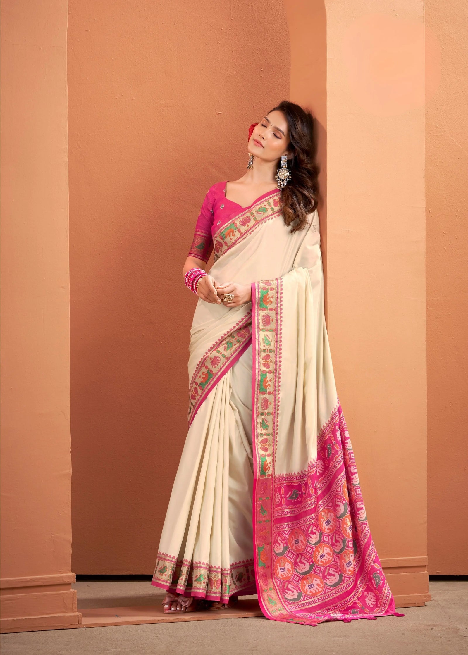 Woman wearing a traditional saree with pink and green patterns against a beige wall.