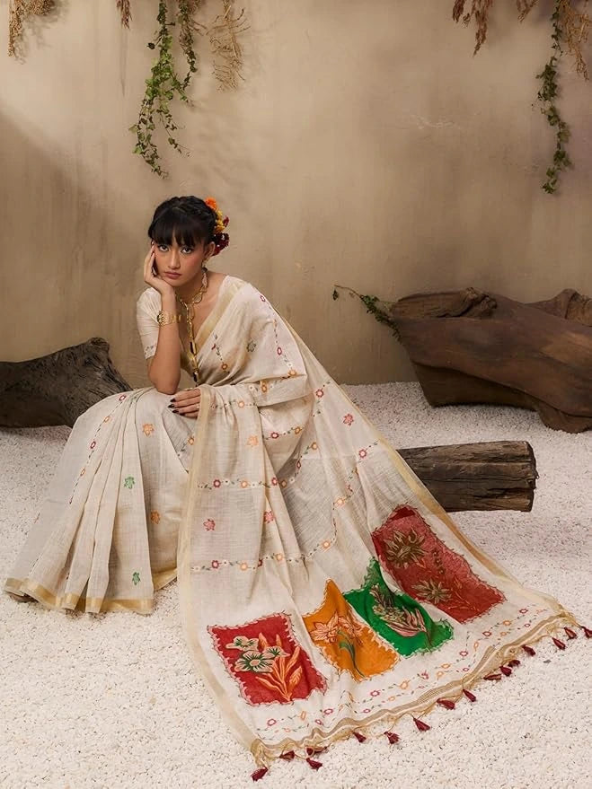 A woman stands elegantly in a soft pastel pink saree with delicate floral embroidery and printed motifs.