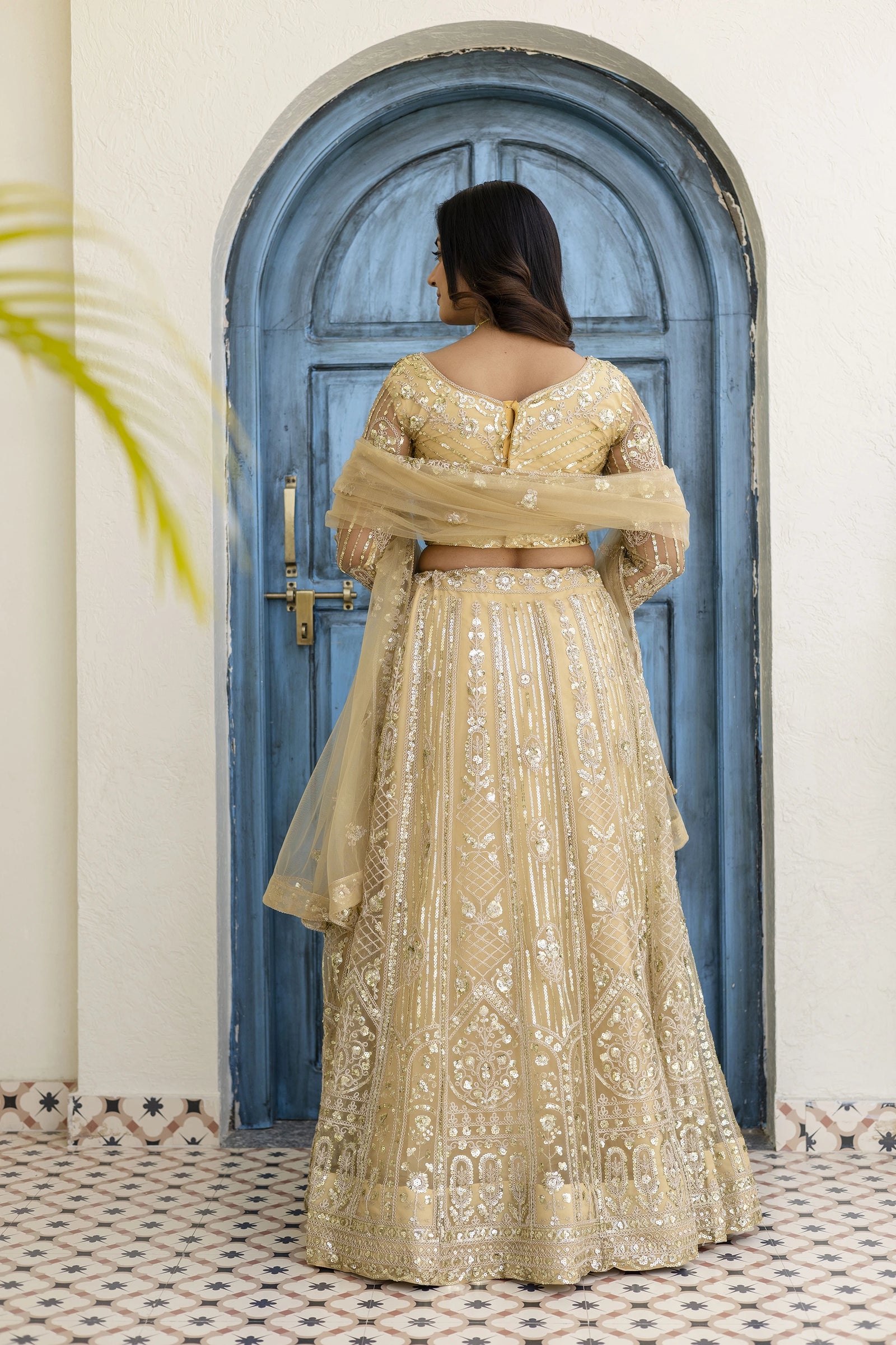 Woman in a traditional beige outfit standing in front of a blue door.