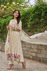 Woman in a cream-colored traditional outfit with floral embroidery standing outdoors.