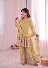 Woman in a light green traditional outfit with embroidery, standing against a white curtain background.