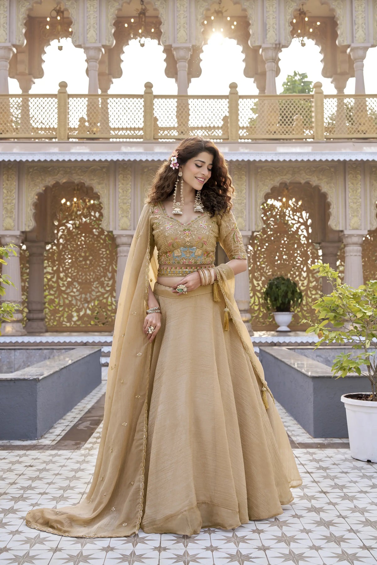 Woman in a traditional beige outfit with floral decorations in an ornate outdoor setting.