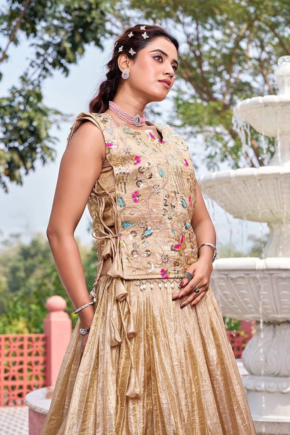 Woman in traditional embroidered outfit standing outdoors with a fountain in the background