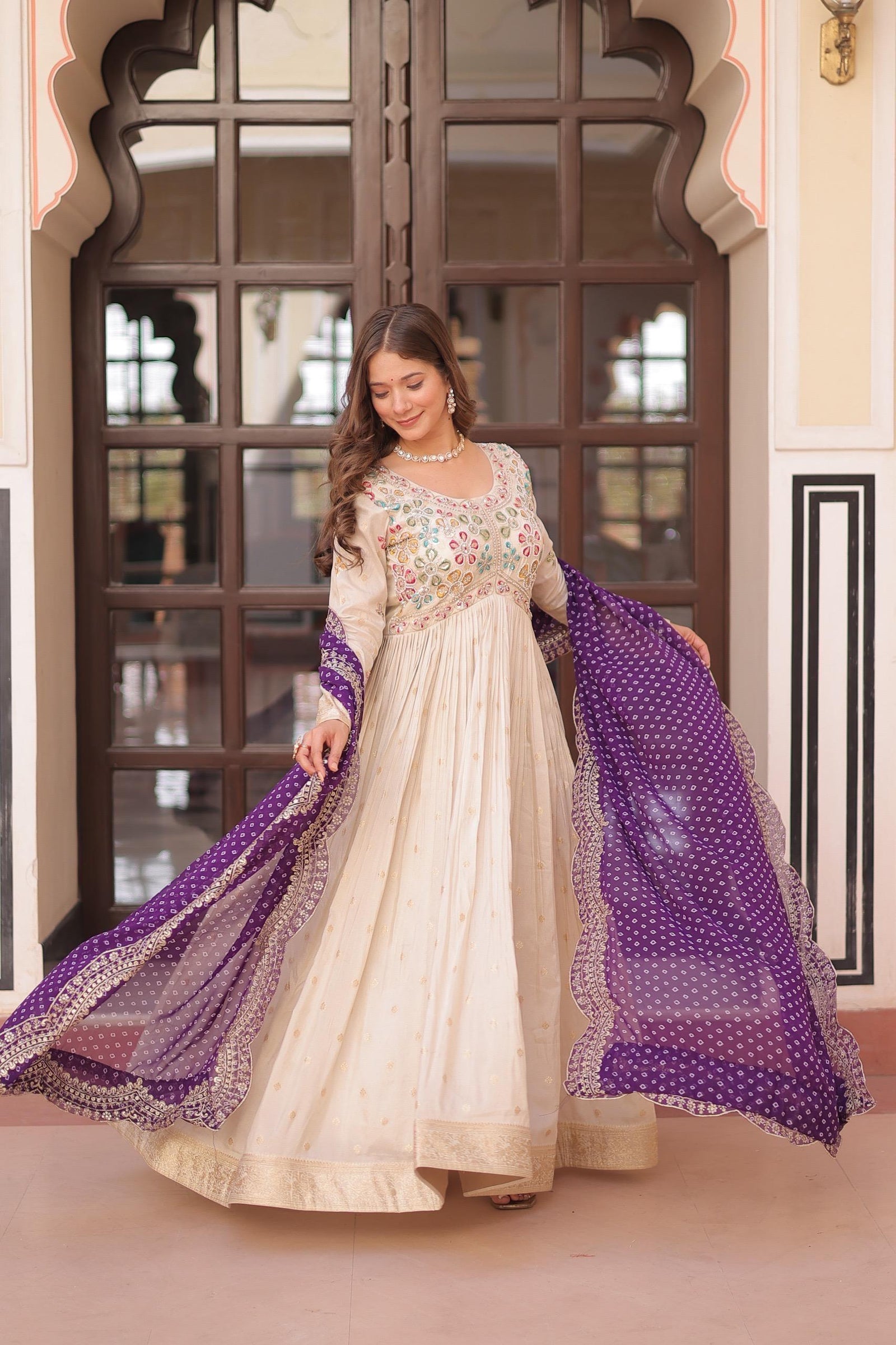 Woman in a traditional outfit with a purple dupatta standing in front of a decorative door.