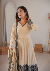Woman wearing a beige dress with black embroidery in a room setting.