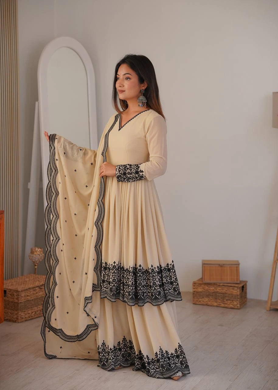 Woman in a beige and black traditional outfit holding a matching dupatta in a room.