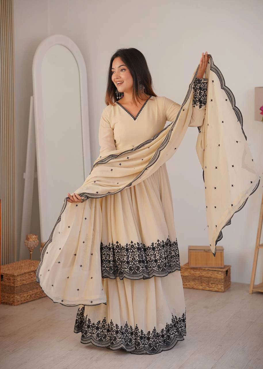 Woman wearing a cream and black embroidered traditional outfit in a room.