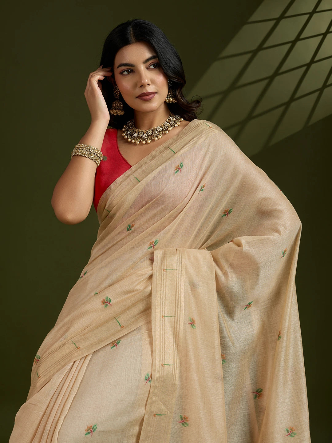 Woman wearing a beige saree with a red blouse against a dark background