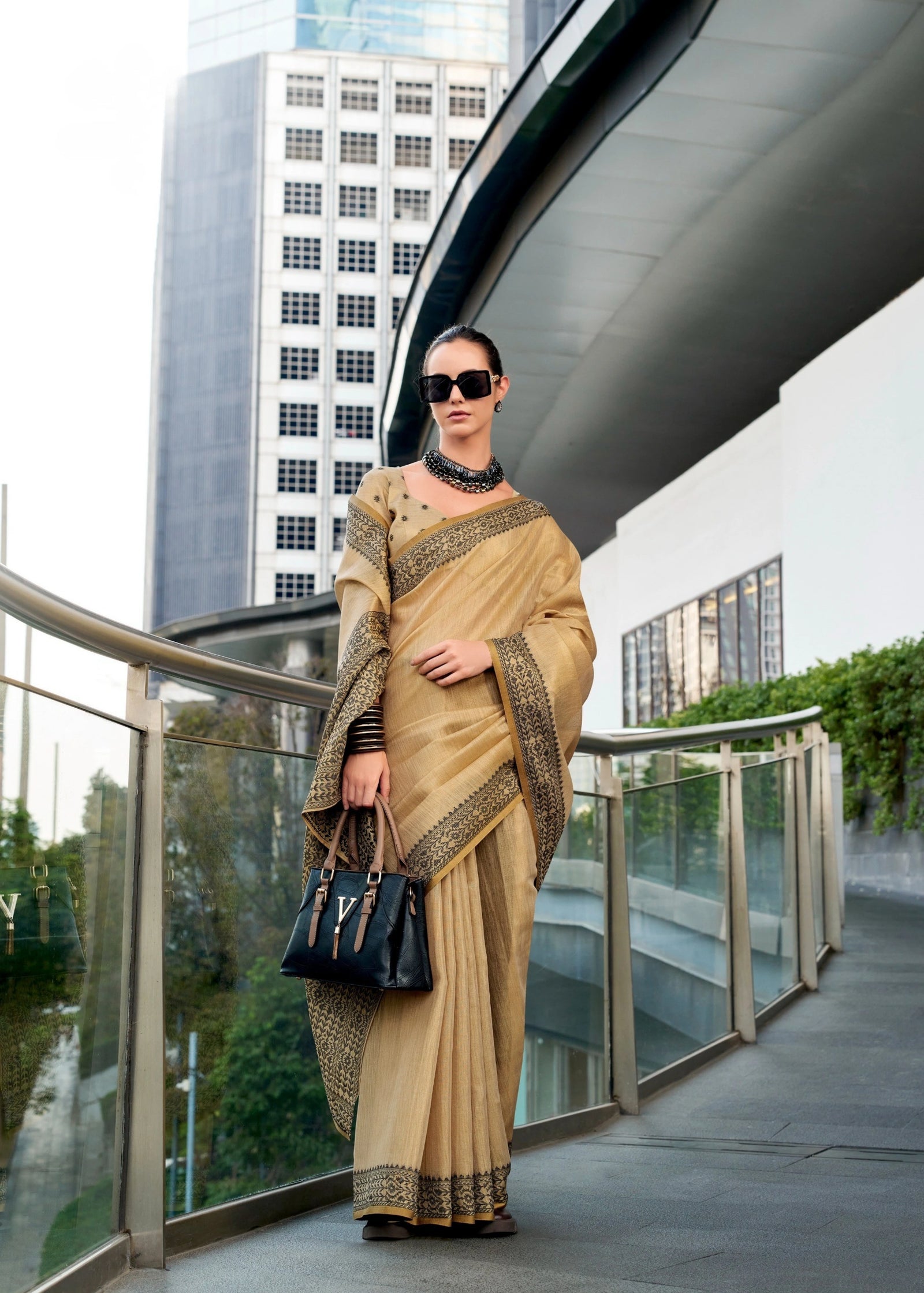 Woman in a beige saree with a black handbag standing in an urban setting.