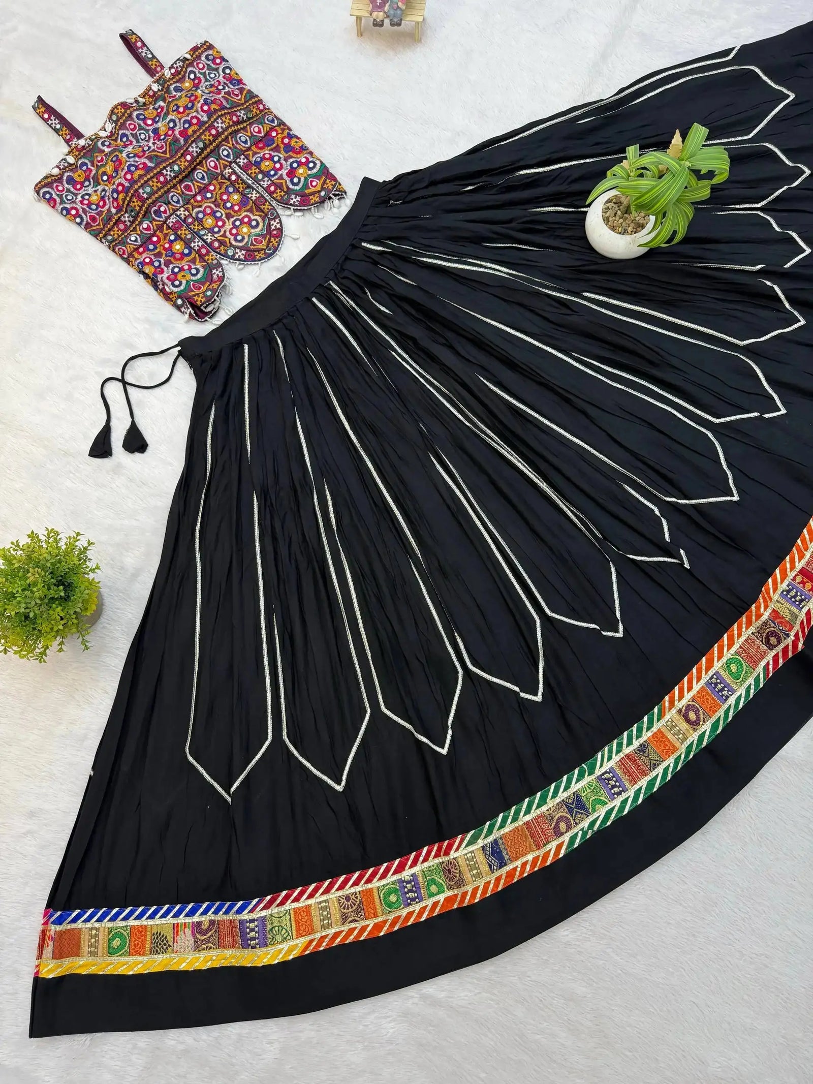 Full spread flat lay of 4-meter black circular lehenga skirt with patola border and Kutchi embroidered choli