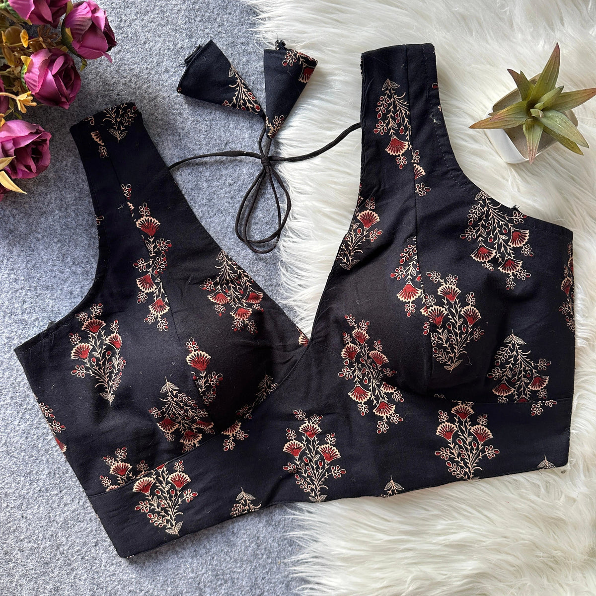 Black embroidered bralette set on a textured surface with flowers and a plant.