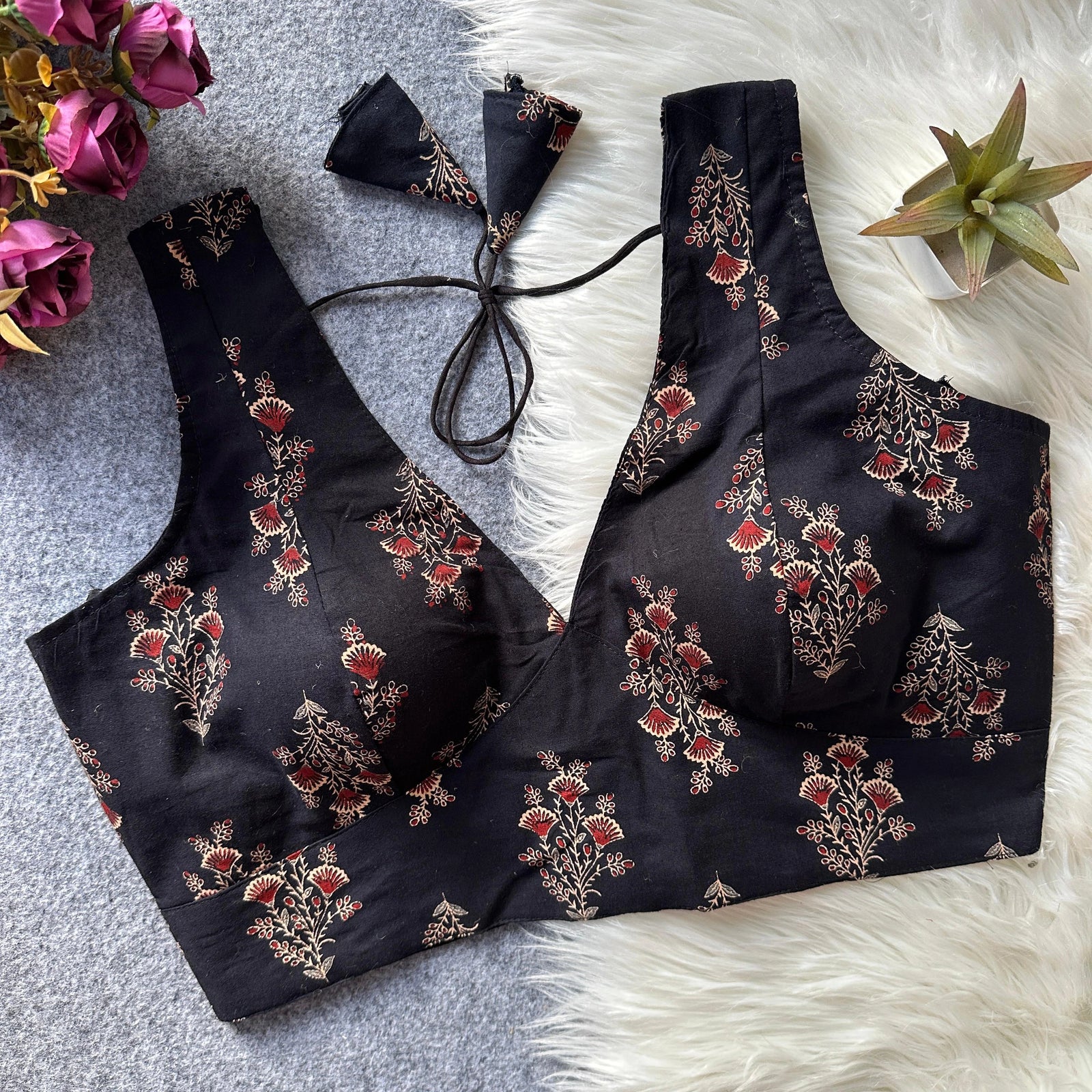 Black embroidered bralette set on a textured surface with flowers and a plant.
