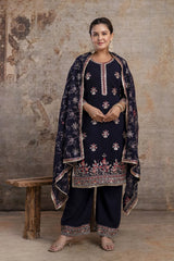Woman wearing a traditional embroidered outfit against a textured wall.