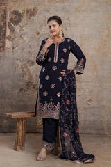 Woman in a navy blue embroidered traditional outfit standing against a textured wall.