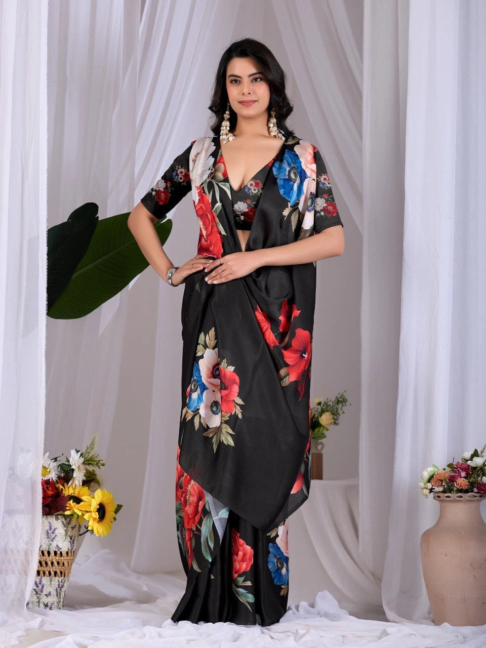 Woman wearing a black floral dress standing against a white curtain with decorative elements.