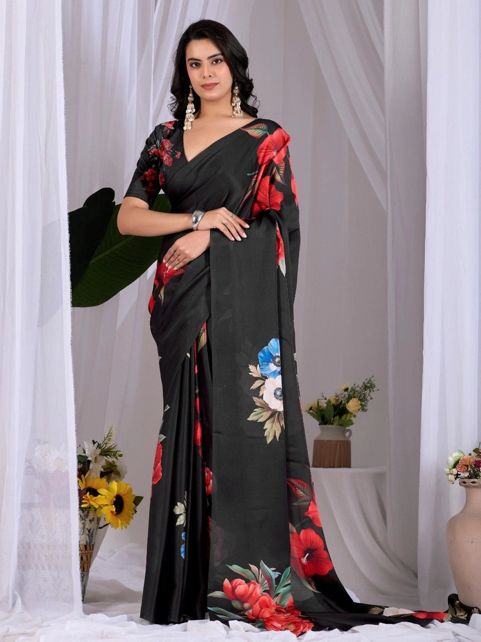 Woman wearing a black saree with floral patterns against a white curtain background