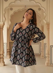A side profile view focusing on the construction of the gathered waist and the pattern alignment on the sleeves. The woman has her hand in her hair, highlighting her silver earrings and the soft, wavy hairstyle.