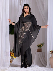 Woman wearing a black saree with leaf patterns in front of white curtains.