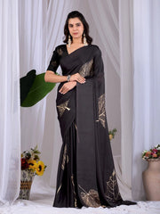 Woman wearing a black saree with gold patterns against a white curtain background